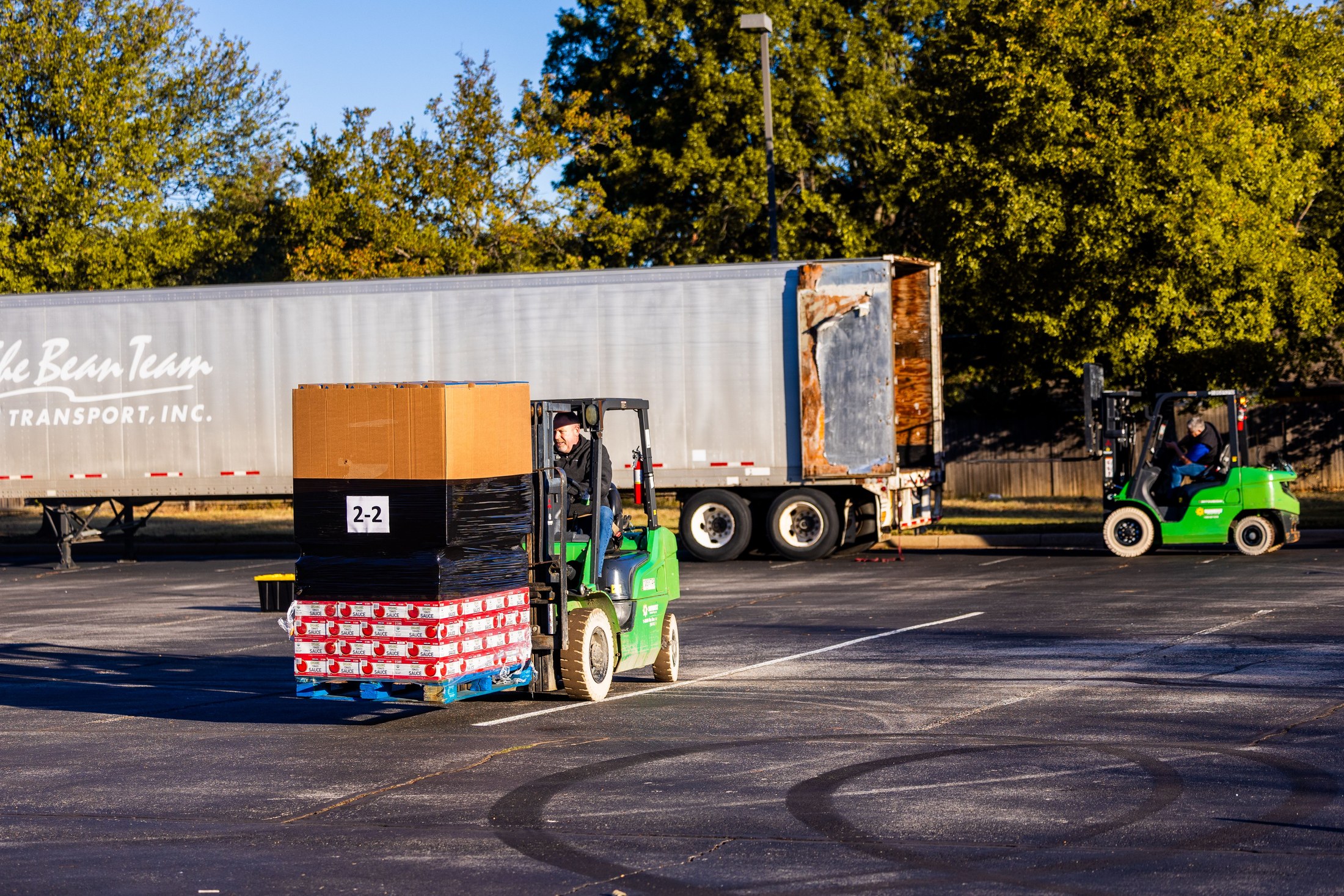 Forklift operators handling pallets beside a trailer in an outdoor loading area.