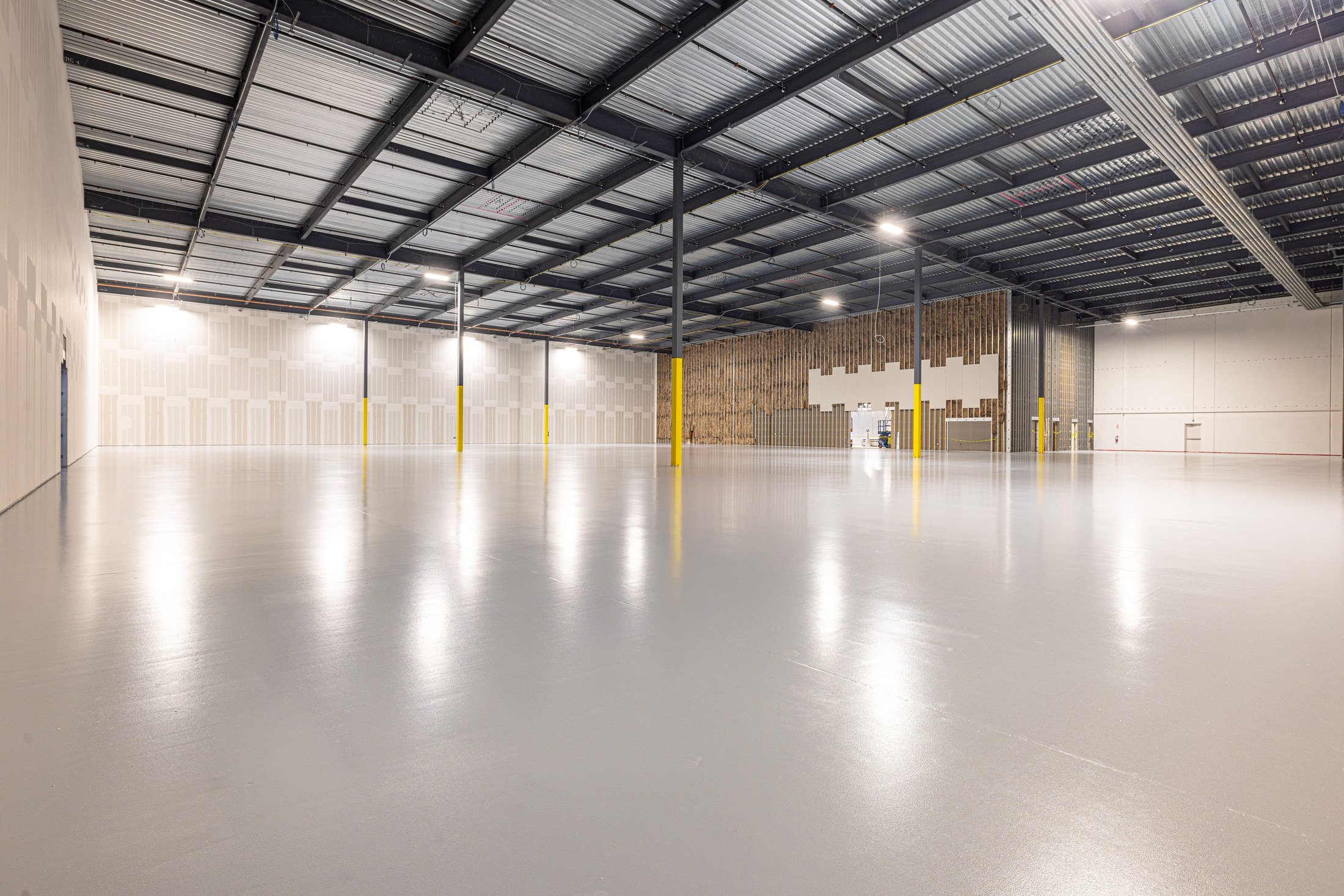 Spacious warehouse interior with structural beams, lighting, and polished concrete floors.