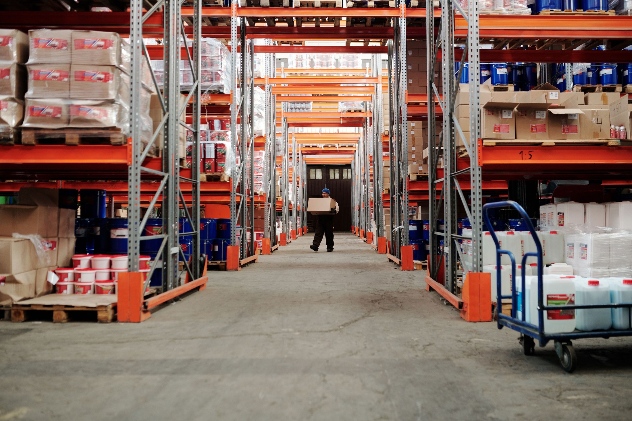 Warehouse worker carrying a cardboard box between storage racks.